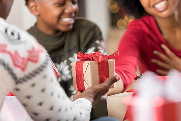 a man and a woman exchange a wrapped gift while a child smiles in the background