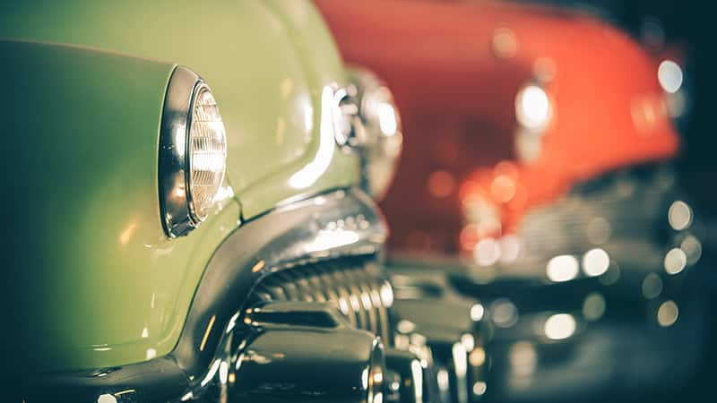 A green vintage car at an auction next to a red one.