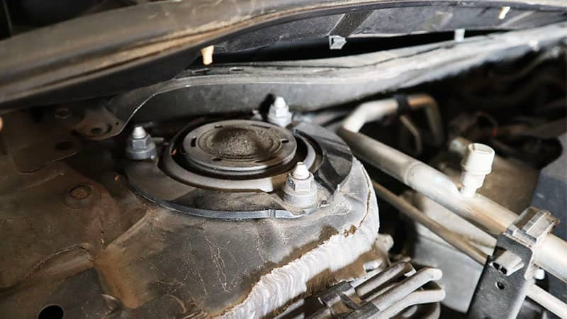 a close up view of the top of the strut tower under the hood, showing the three nuts that secure the strut to the vehicle body