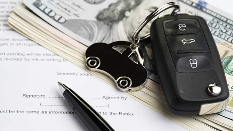 A car key and money sit on top of signed sale documents.